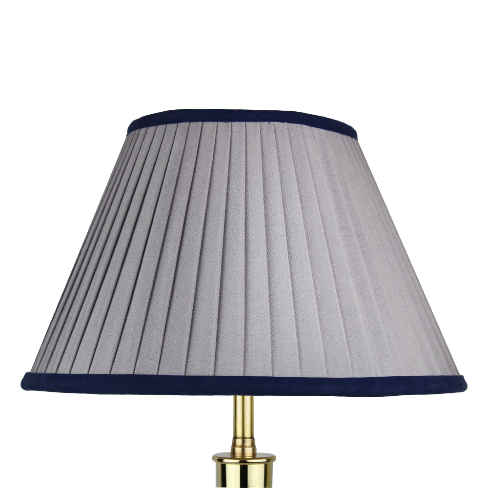 A pleated gray lampshade with a navy blue trim, mounted on a brass base.