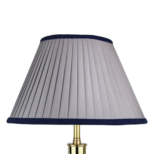A pleated gray lampshade with a navy blue trim, mounted on a brass base.