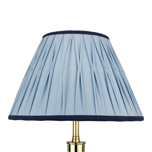 A vintage blue Empire style silk lampshade with smocked pleats, displayed on a brass lamp base.