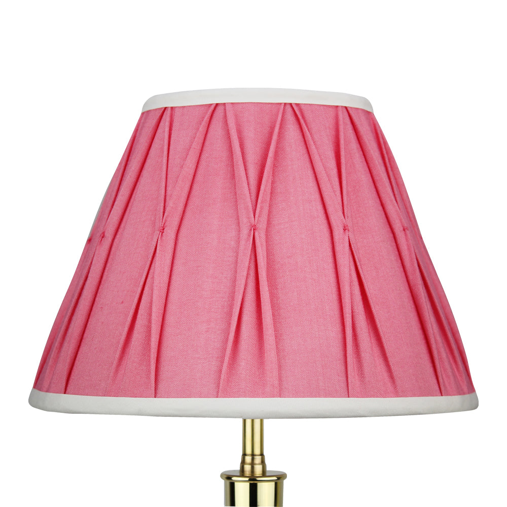 A pink silk Empire lampshade with pleated detail and a white trim, displayed on a gold-colored lamp.