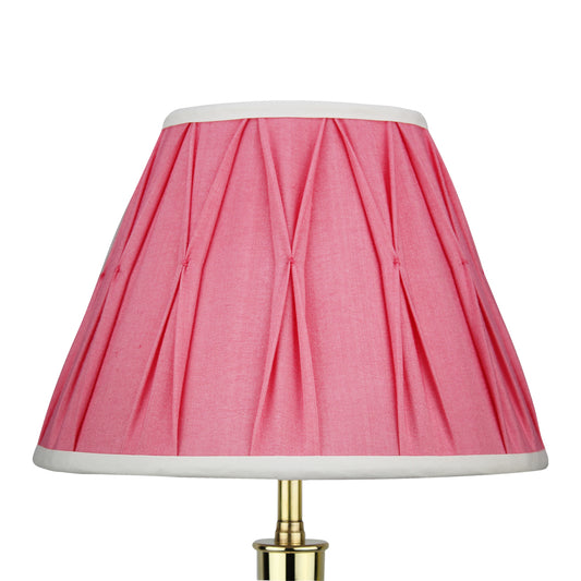 A pink silk Empire lampshade with pleated detail and a white trim, displayed on a gold-colored lamp.
